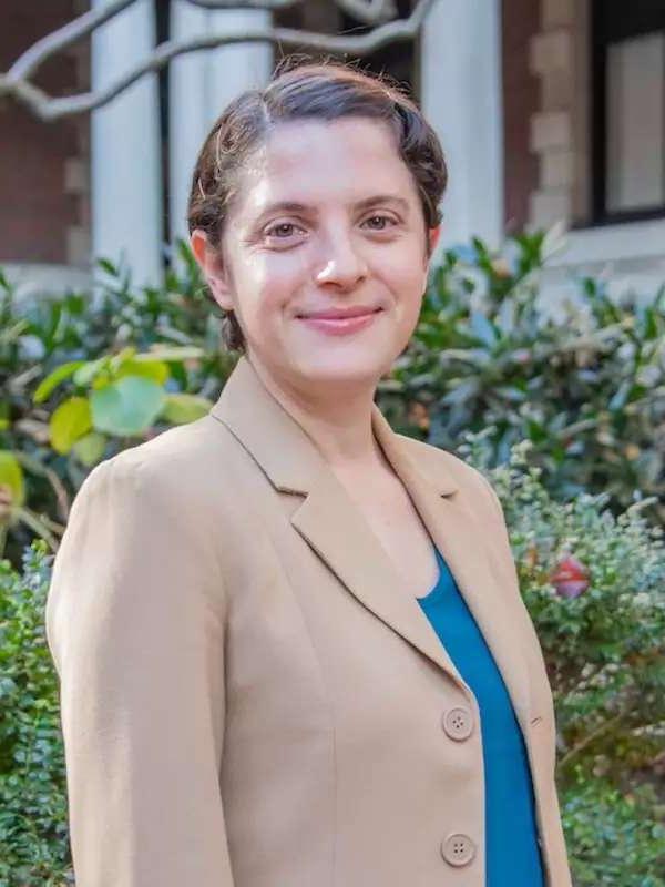 green background, woman wearing light brown blazer, blue shirt and short brown hair